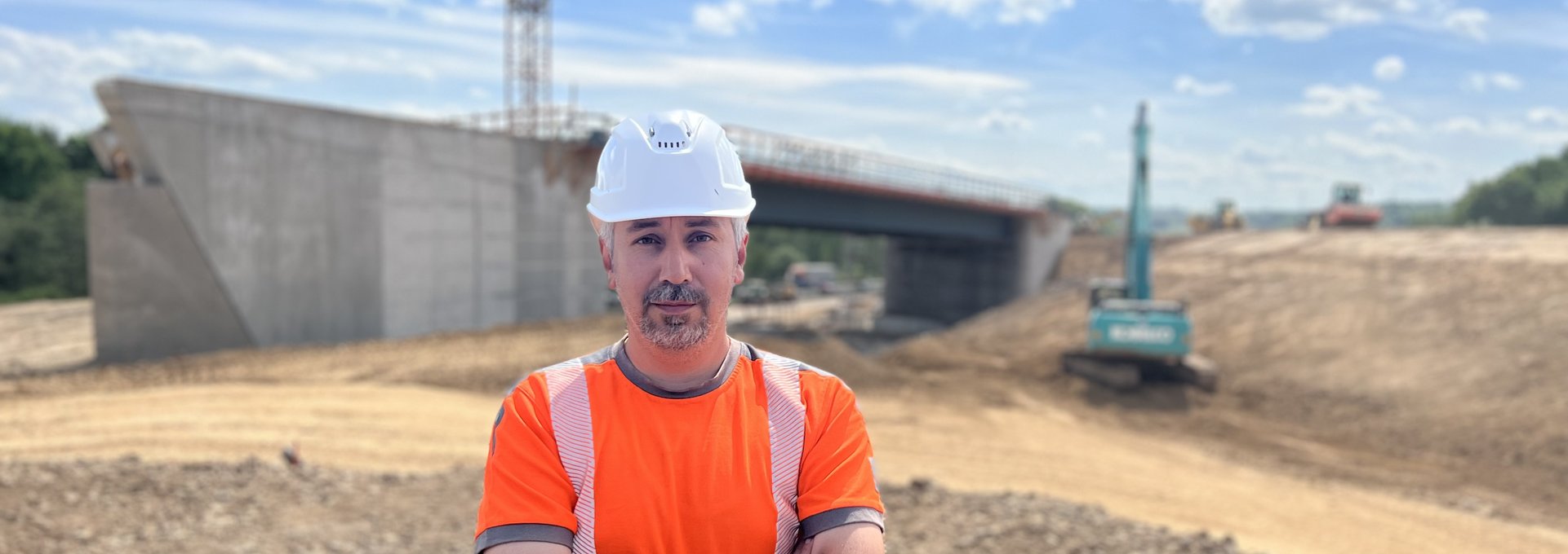 Ein Mann steht im Bauarbeiter-Outfit auf einer Baustelle.