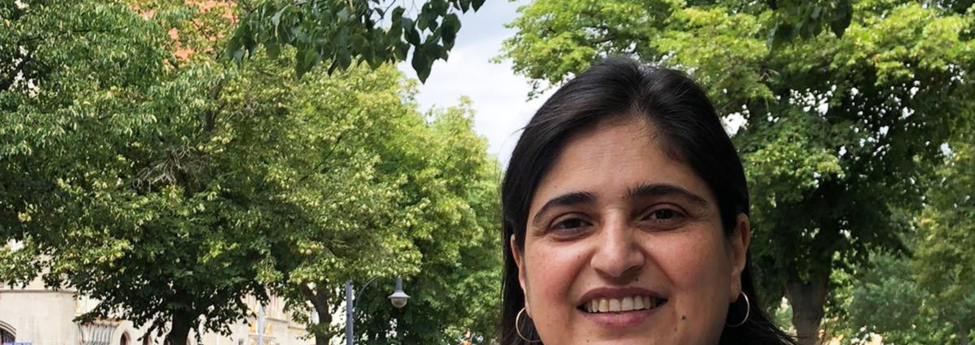 Eine Frau steht in einem Park. Sie trägt ein blaues Poloshirt.