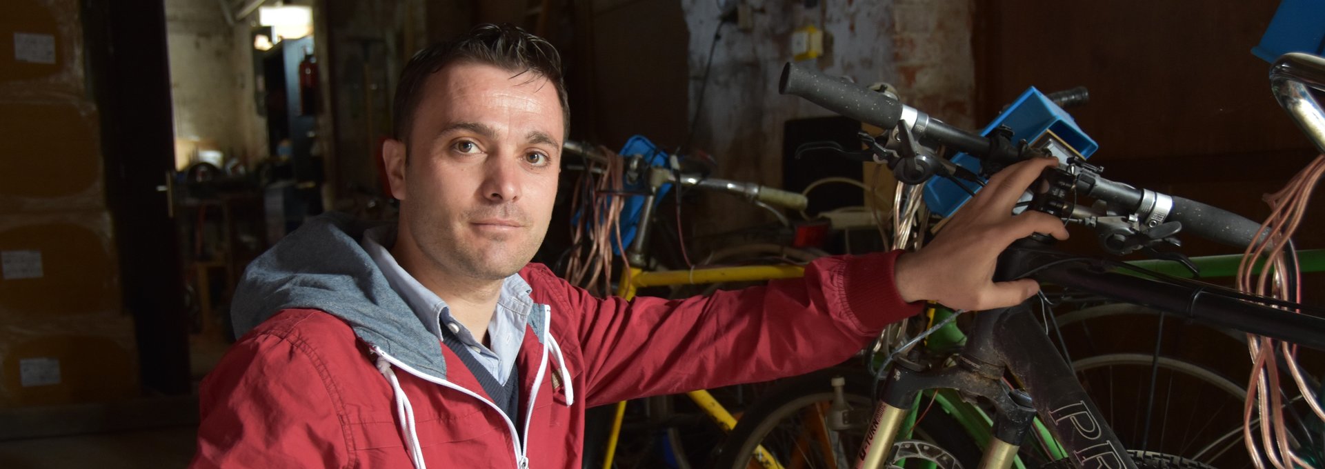 Ein junger Mann mit roter Jacke kniet for einem Fahrrad.