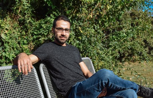 Ein junger Mann sitzt auf einer Parkbank und die Sonne scheint.