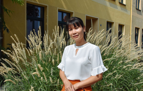 Eine schlanke Frau aus Vietnam lächelt freundlich in die Kamera. Sie trägt eine weiße Bluse und hat schwarze Haare.
