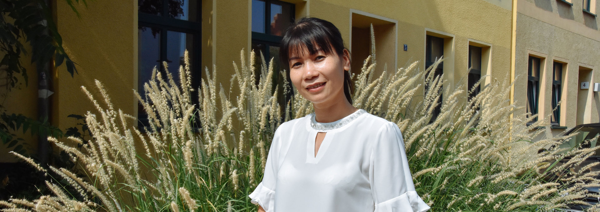 Eine schlanke Frau aus Vietnam lächelt freundlich in die Kamera. Sie trägt eine weiße Bluse und hat schwarze Haare.