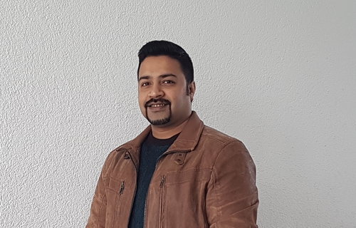 Ein junger Mann steht vor einer weißen Wand.