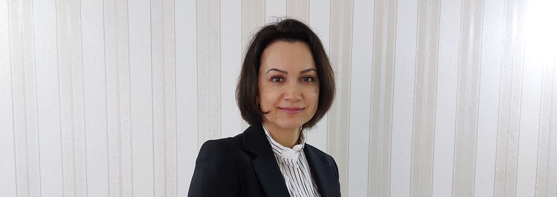 Eine junge Frau steht im Business-Outfit für einer Wand.