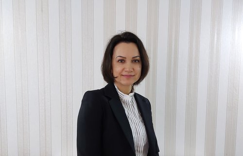 Eine junge Frau steht im Business-Outfit für einer Wand.