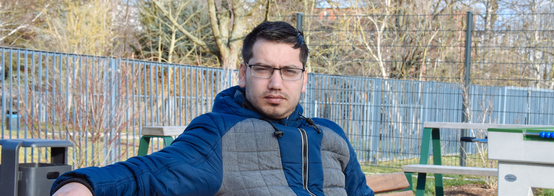 Ein junger Mann sitzt auf einer Bank und schaut ernst.