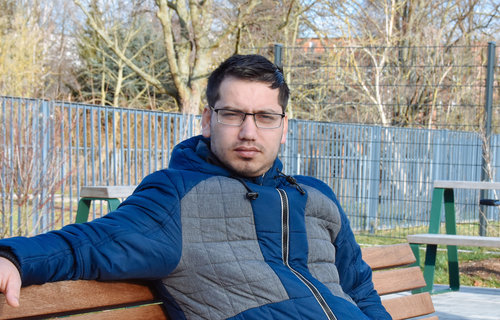 Ein junger Mann sitzt auf einer Bank und schaut ernst.