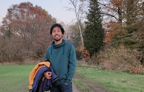 Ein junger Mann aus Indien steht auf einem Waldweg.