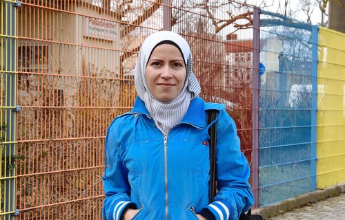 Eine junge Frau mit Kopftuch steht vor einem bunten Zaun