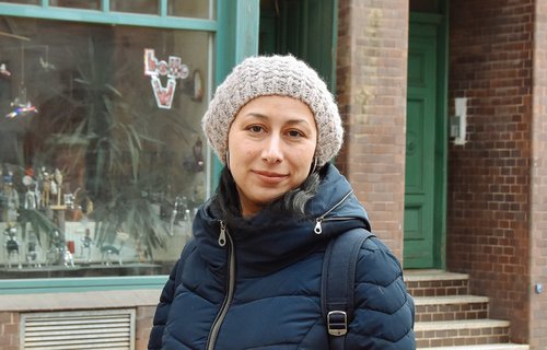 Eine junge Frau steht auf der Straße. Sie trägt eine dicke Jacke und eine Mütze.