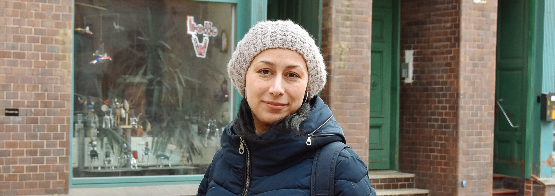 Eine junge Frau steht auf der Straße. Sie trägt eine dicke Jacke und eine Mütze.
