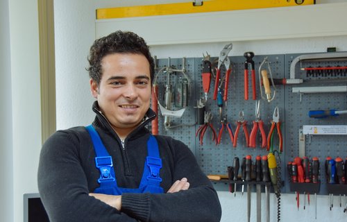 Ein junger Mann in Arbeitskleidung steht vor einer Werkbank.