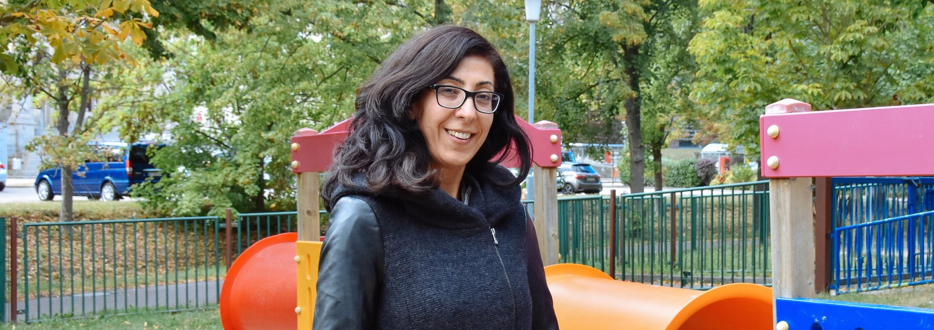 Eine junge Frau steht auf einem Kinderspielplatz. Sie lächelt. 