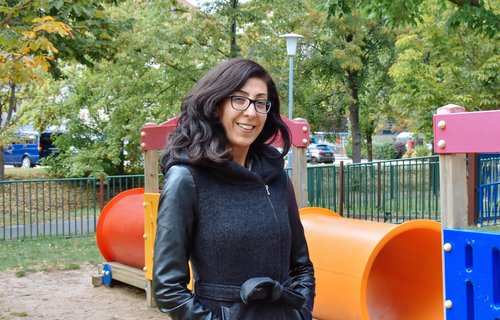 Eine junge Frau steht auf einem Kinderspielplatz. Sie lächelt. 
