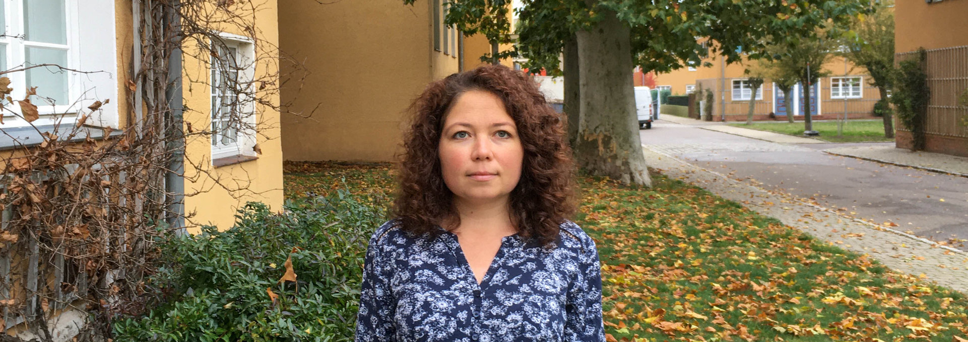 Eine junge Frau steht im Vorgarten ihres Hauses.