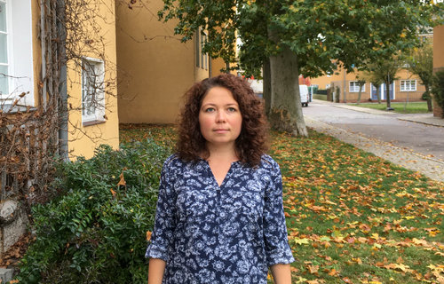 Eine junge Frau steht im Vorgarten ihres Hauses.