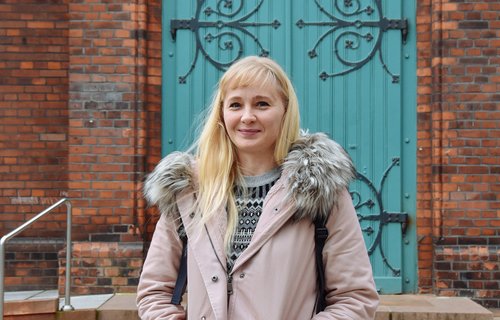 Ein junge blonde Frau steht vor einer Kirche.