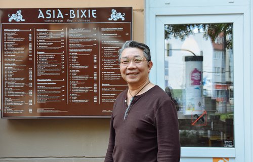 Ein ältere Mann steht vor seinem asiatischen Restaurant.
