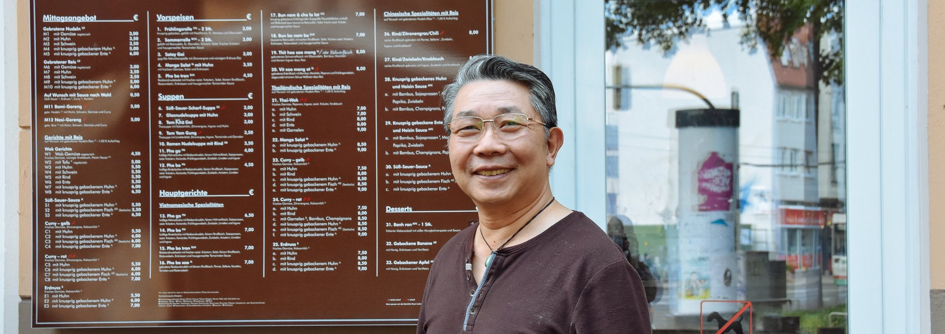 Ein ältere Mann steht vor seinem asiatischen Restaurant.