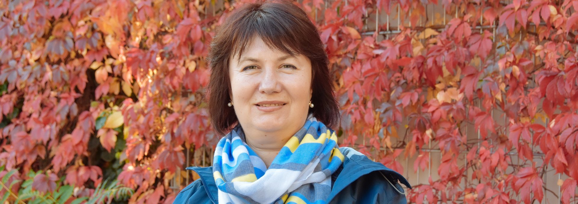 Eine Frau steht vor einer bewachsenen Häuserwand. Es ist Herbst und die Farben leuchten.