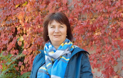 Eine Frau steht vor einer bewachsenen Häuserwand. Es ist Herbst und die Farben leuchten.