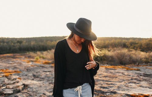 Eine junge Frau strägt einen großen Hut im Sonnenuntergang.