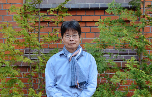 Ein älter Herr aus Vietnam steht vor einer Mauer.